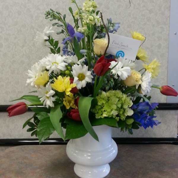 Mixed bouquet of daisies, tulips, and roses in a white vase