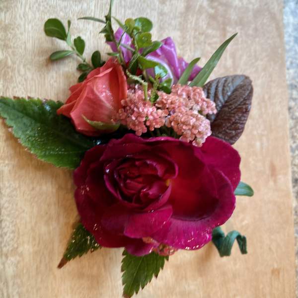 Small floral corsage with red and pink roses on a wooden surface