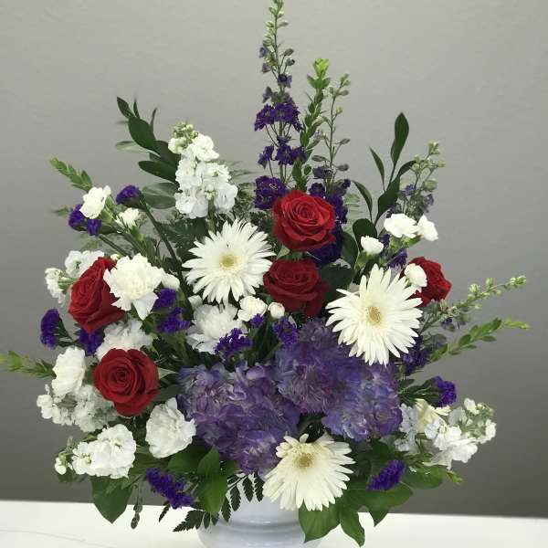 Red roses, white gerberas, and purple hydrangeas in a white vase