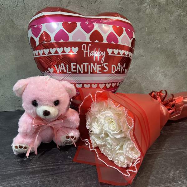 Pink teddy bear, heart balloon, and white rose bouquet on a table