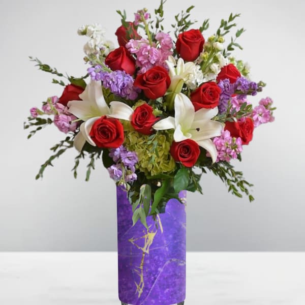 Bouquet of red roses, white lilies, and pink flowers in a purple vase