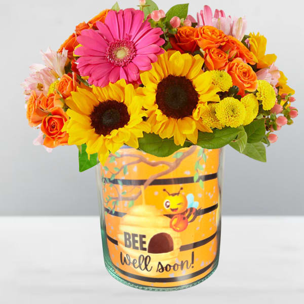 Bright mixed bouquet in a glass vase with a bee well soon label