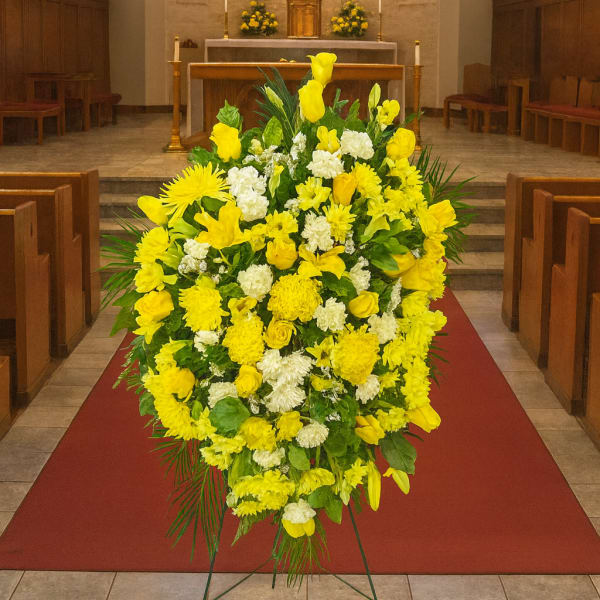 Large yellow and white funeral spray on a stand in a church aisle