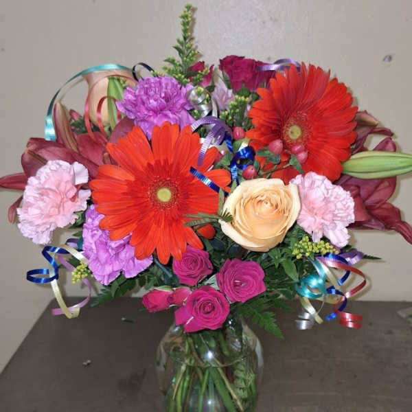 Colorful bouquet of gerbera daisies, roses, and carnations in a glass vase