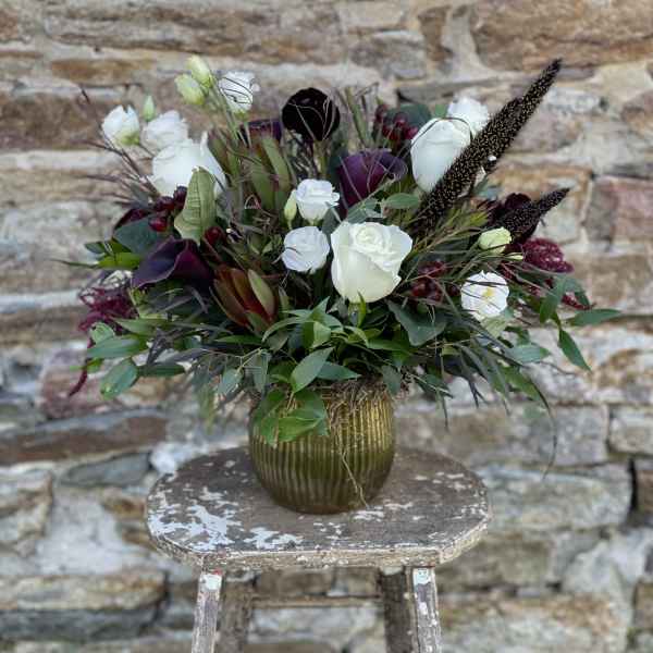 White roses and dark purple flowers in a ribbed gold vase