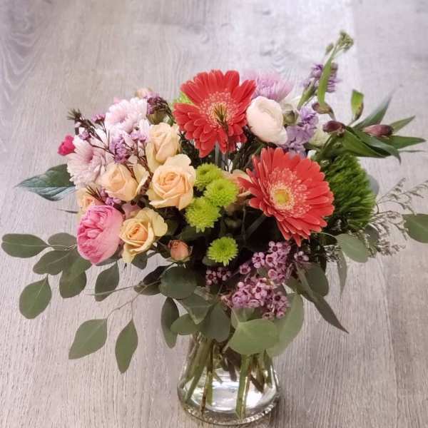 Mixed bouquet of pink, peach, and red flowers in a glass vase