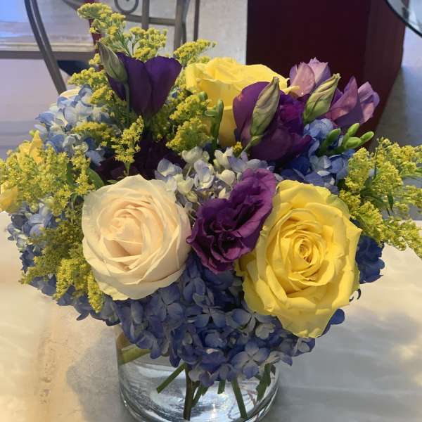 Bouquet of yellow, white, purple, and blue flowers in a clear glass vase