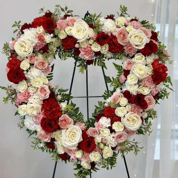 Heart-shaped floral wreath of red, pink, and white roses on a stand