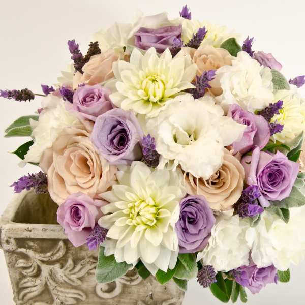 Bouquet of lavender, cream, and blush flowers in a decorative stone planter
