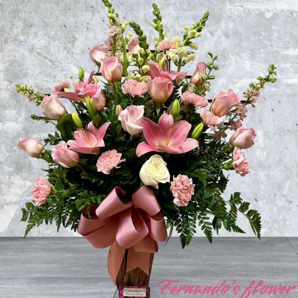 Tall pink and white flower arrangement with lilies, roses, and carnations in a vase with a pink bow