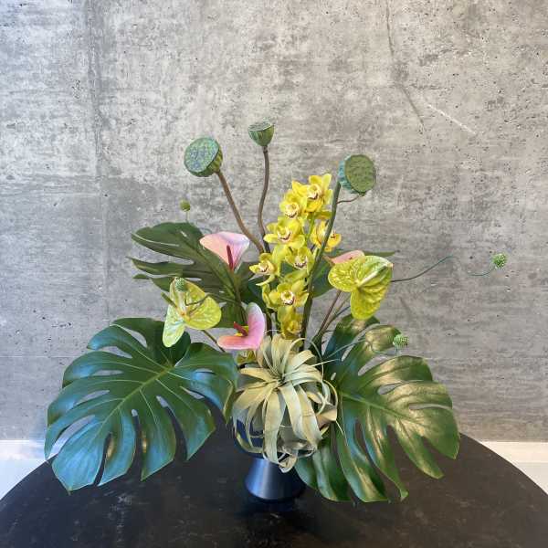 Tropical arrangement with yellow orchids and large monstera leaves in a vase