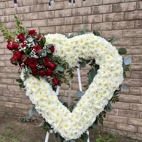 Heart-shaped floral wreath with white chrysanthemums and red roses on a stand