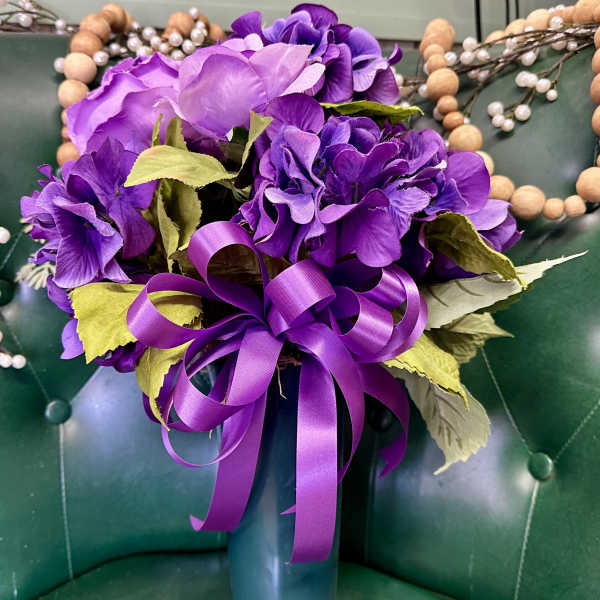 Purple floral arrangement in a teal vase with a ribbon bow