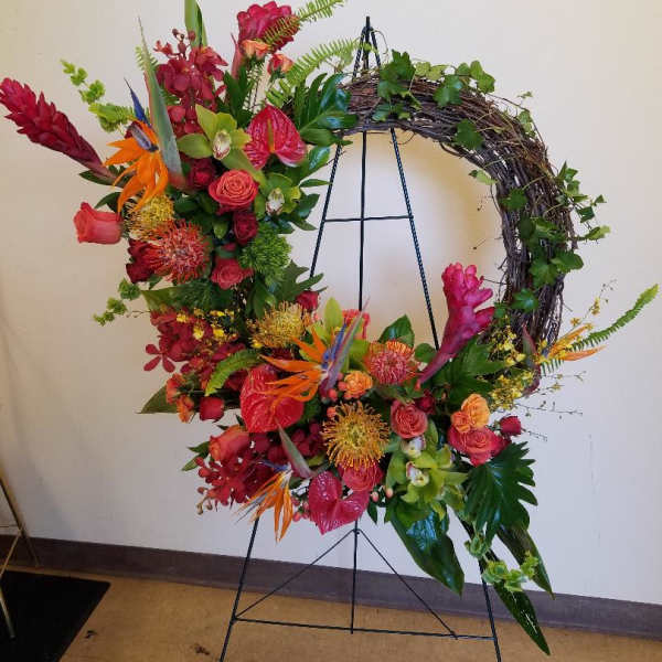 Large floral wreath on a metal stand with red, orange, and pink blooms