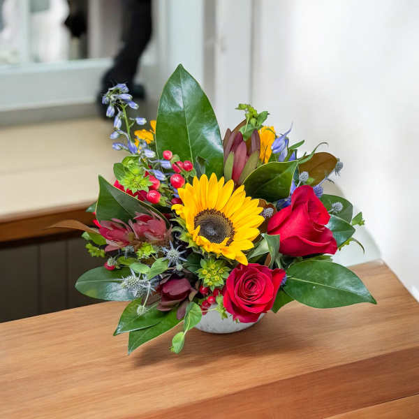 Bouquet with a sunflower and red roses in a low white vase