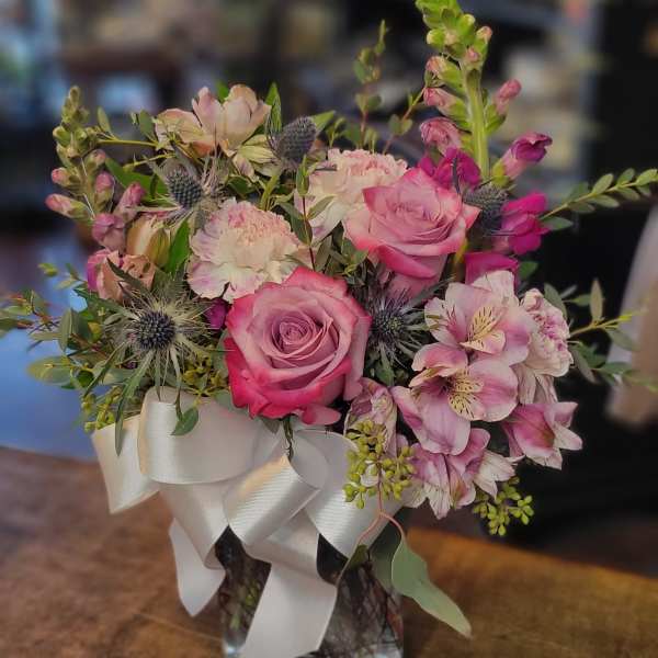 Pink roses and mixed blooms arranged in a glass vase with a white ribbon