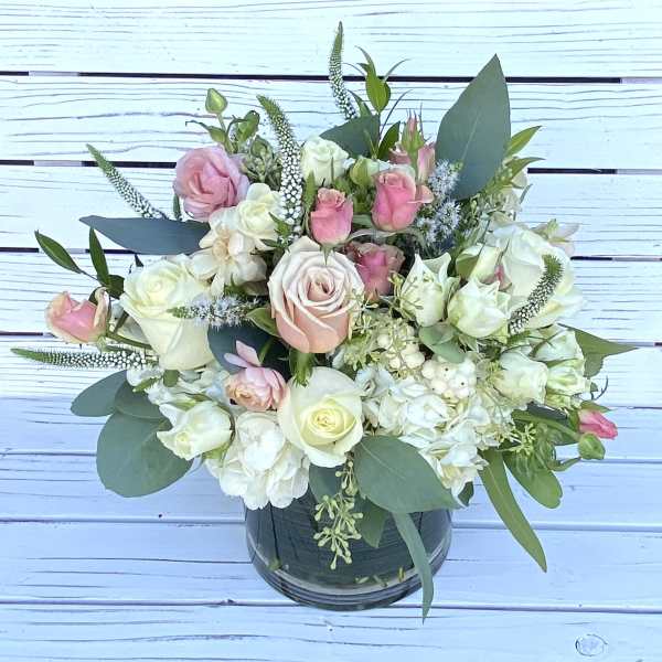 Low arrangement of white and blush roses and hydrangeas in a clear glass cylinder vase