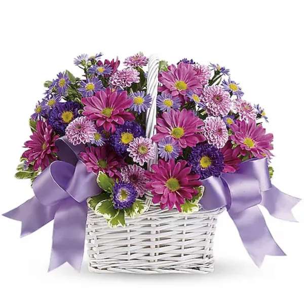Purple and pink daisy bouquet in a white wicker basket with lavender ribbon