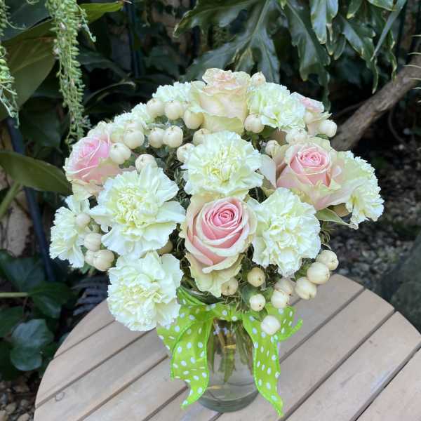 Bouquet of pink roses and white carnations in a glass vase with a green ribbon
