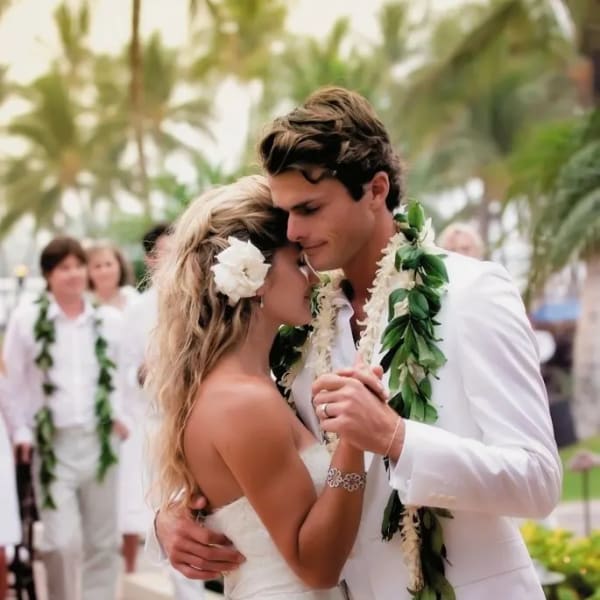 Bride and groom in white with floral leis and a white flower in her hair