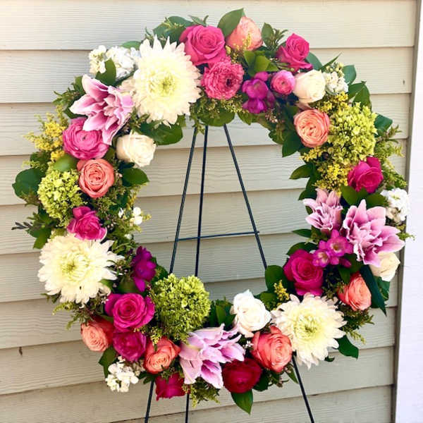 Heart-shaped floral wreath with pink, white, and peach blooms on a black stand