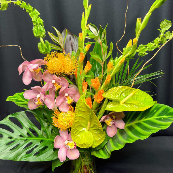 Tropical arrangement with pink orchids, yellow pincushion blooms, and anthuriums in a glass vase