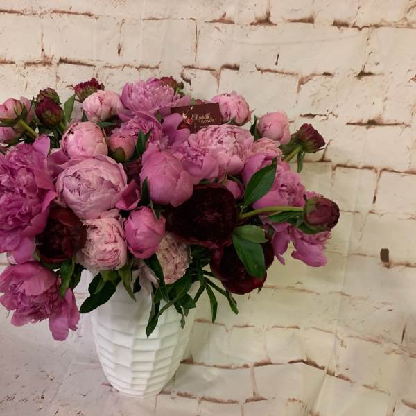 Lush arrangement of pink and burgundy peonies in a textured white vase