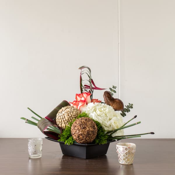 Floral arrangement with white hydrangeas, red-edged roses, and decorative pods in a black container