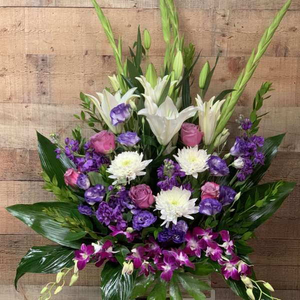 Tall bouquet of white lilies, purple orchids, and pink roses in a vase