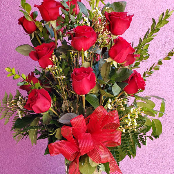 Red roses arranged in a clear glass vase with a red ribbon bow