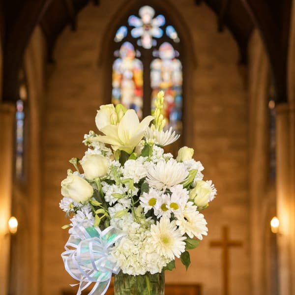 White floral arrangement in a clear glass vase with a ribbon bow