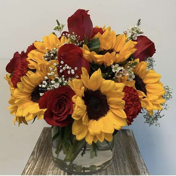 Bouquet of red roses and yellow sunflowers in a clear glass vase