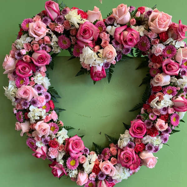 Heart-shaped floral wreath of pink and white roses on a green wall
