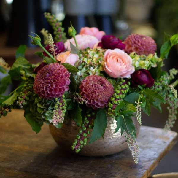 Low floral arrangement with pink and burgundy blooms in a metal bowl