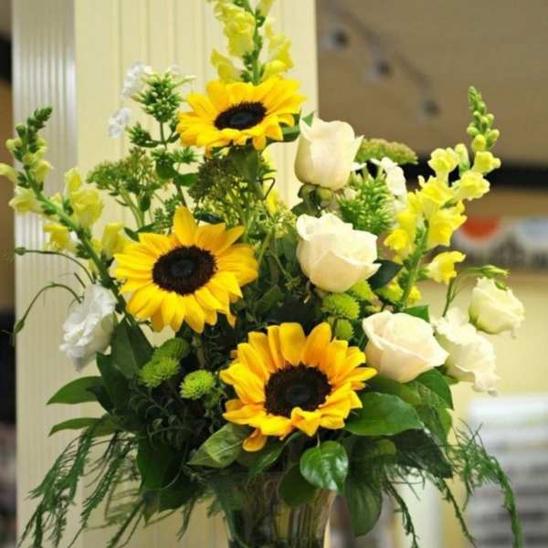 Tall arrangement of yellow sunflowers and white roses in a clear glass vase
