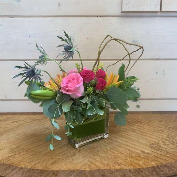 Pink roses and lilies in a square glass vase with airy greenery
