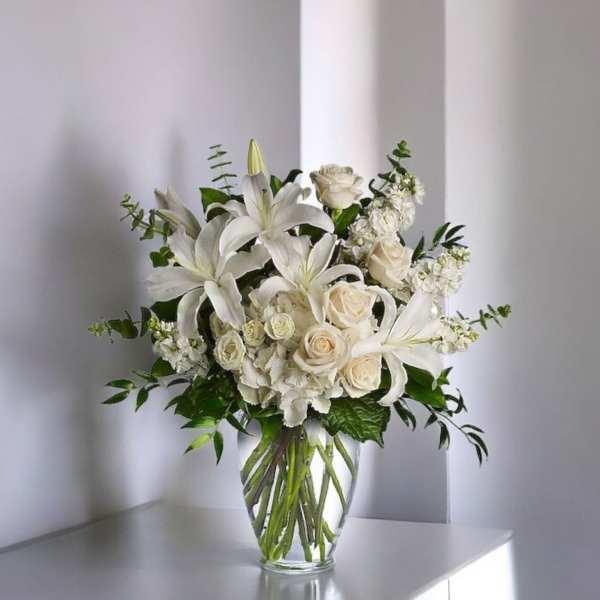 White lilies and cream roses arranged in a clear glass vase