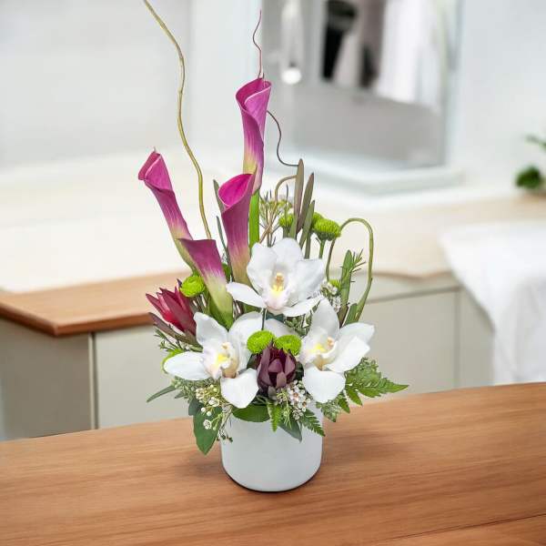 White vase arrangement with pink calla lilies, white orchids, and green accents