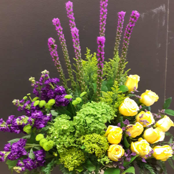 Yellow roses and purple flowers in a white pedestal vase