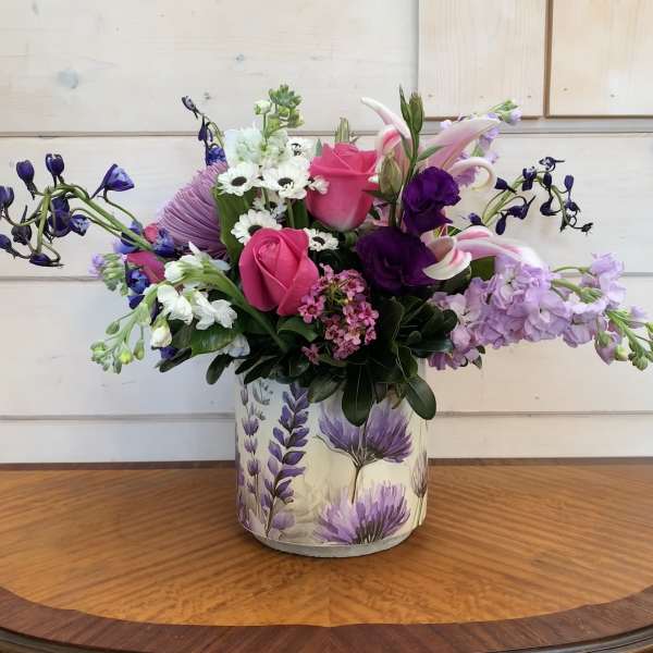 Mixed bouquet of pink roses, lilies, and purple flowers in a floral tin