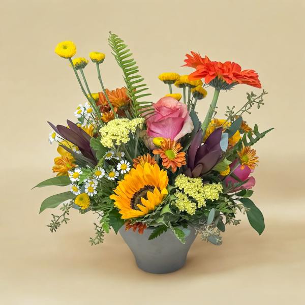 Mixed bouquet with sunflowers, roses, and daisies in a gray vase