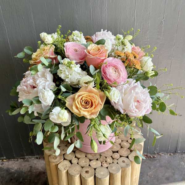 Arrangement of pink and peach roses, ranunculus, and white blooms in a pink round container