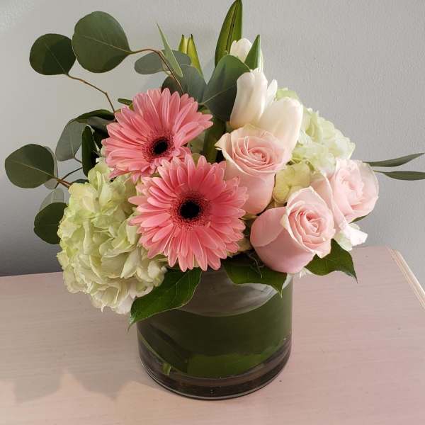 Pink gerbera daisies and roses in a glass vase with pale hydrangea