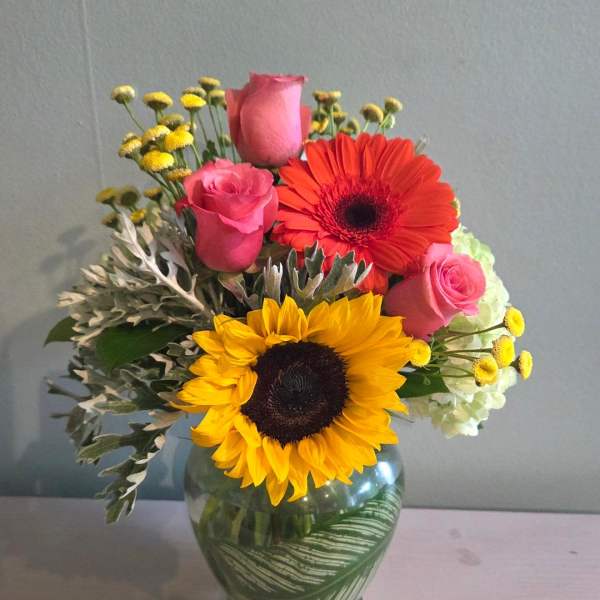 Bouquet of pink roses, sunflowers, and a red gerbera daisy in a glass vase