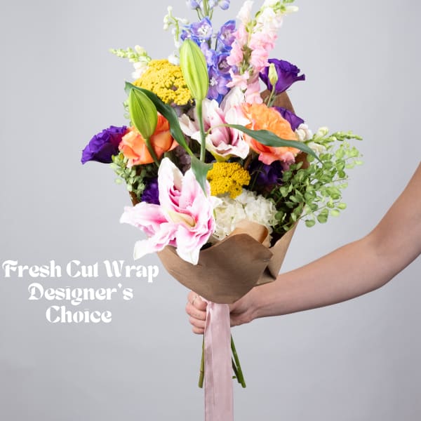 Hand-tied bouquet of mixed flowers in brown paper with a pink ribbon