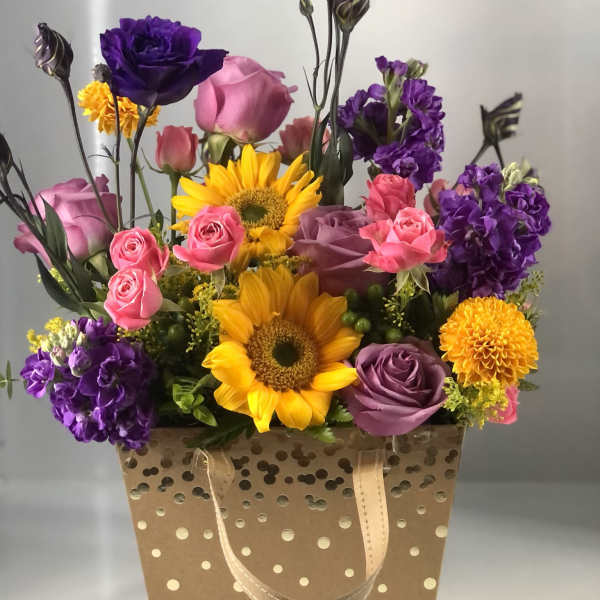Mixed bouquet in a polka-dot gift bag with sunflowers, roses, and purple blooms