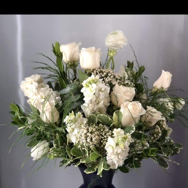 White roses and blooms arranged in a dark blue vase