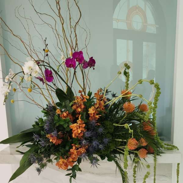 Tall floral arrangement with orchids, orange blooms, and twisting branches