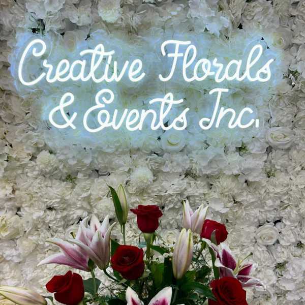 Red roses and pink lilies in front of a white floral wall with neon text