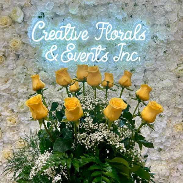 Yellow roses arranged before a white floral wall with a glowing sign